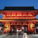 A large red building illuminated at night, featuring a prominent gate that stands out against the dark sky.